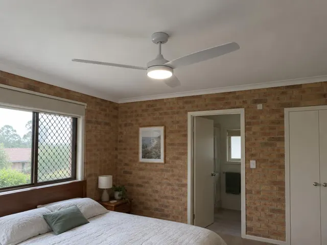 Ceiling fan with light in a brick-walled bedroom with bed and window in Metford