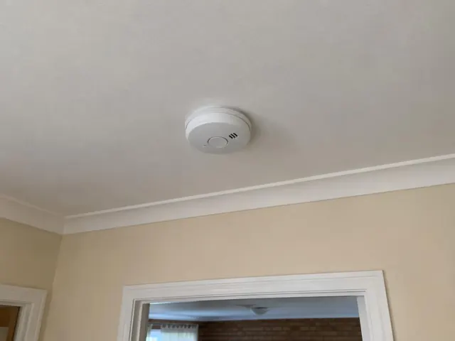 Ceiling smoke alarm on a painted plaster ceiling above a doorway in a beige interior in Metford